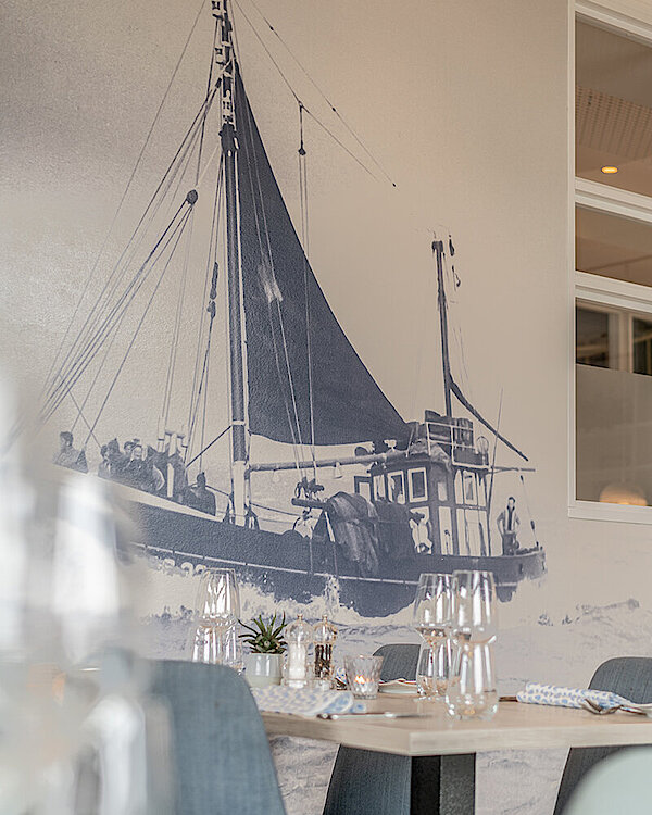 Gedeckter Tisch mit Weingläsern vor maritimer Wandgestaltung im Restaurant Deichperle